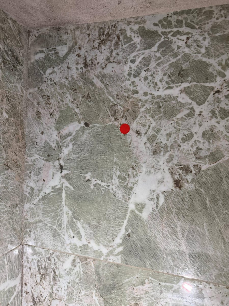 Red marker identifying a washroom wall tile acoustic-sounding test location